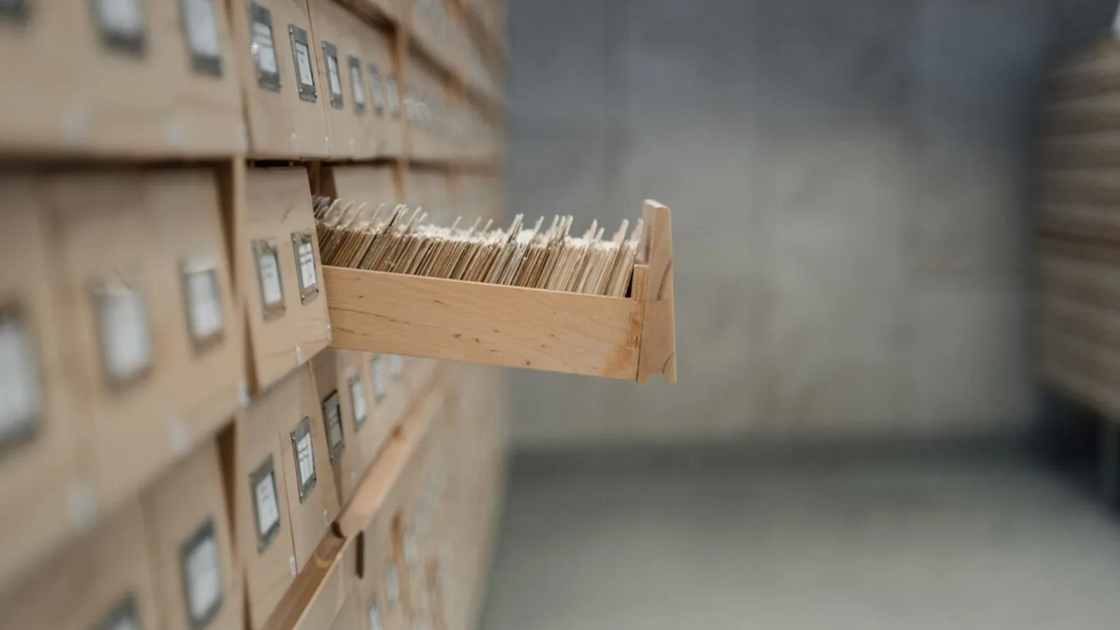 Drewniana kartoteka biblioteczna z wysuniętą szufladą pełną kart katalogowych