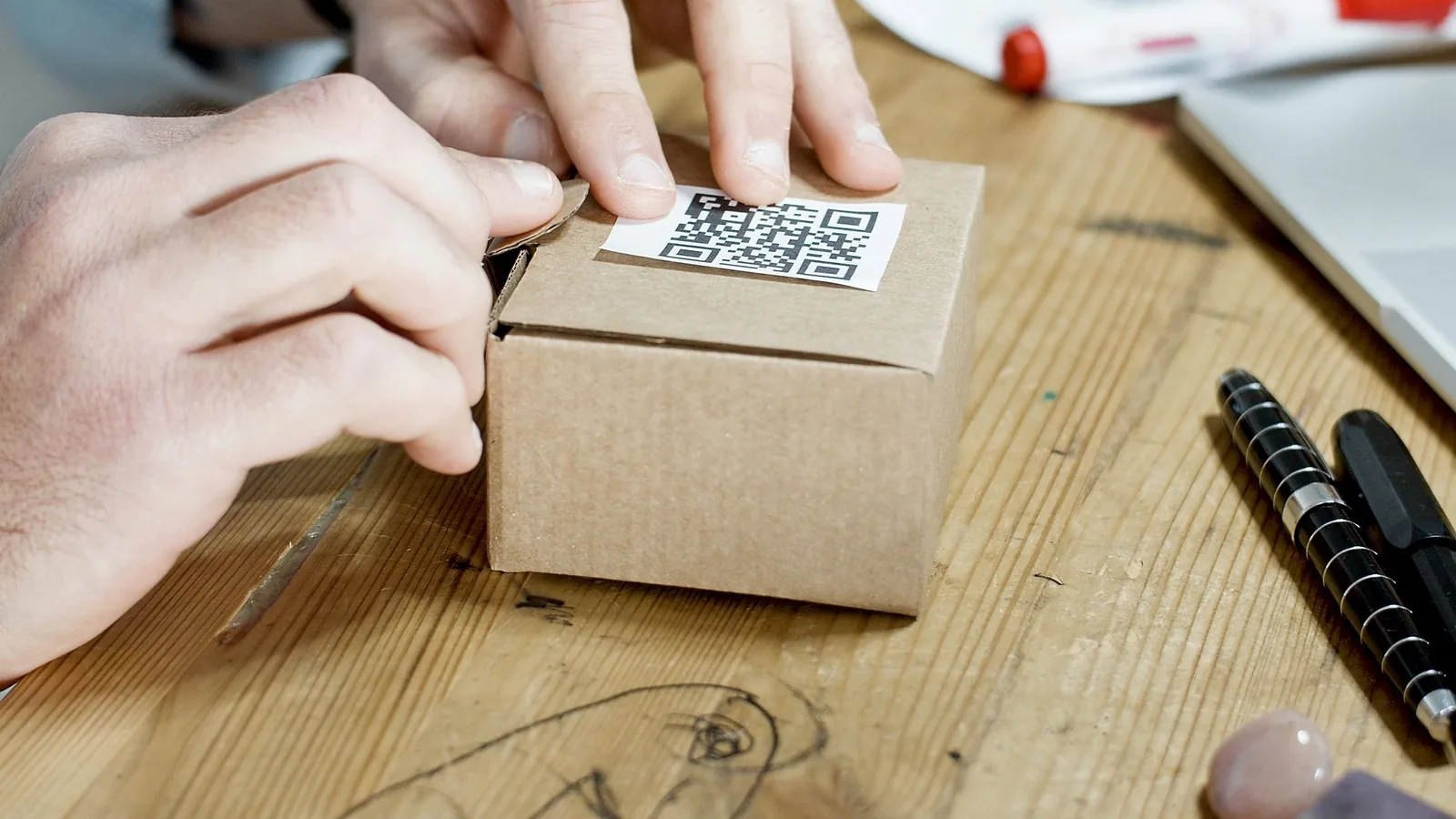 Close-up of hands packing a box with a QR code, symbolizing online business services.