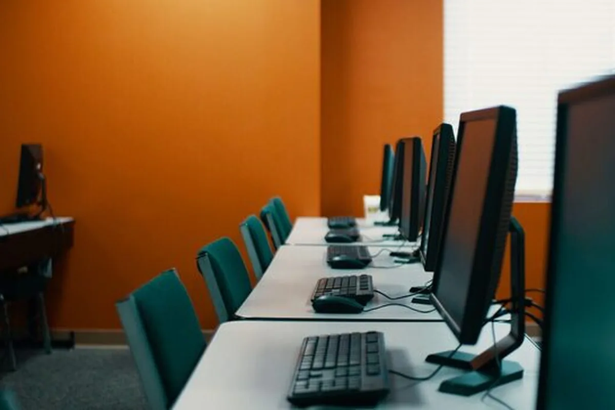 Rząd monitorów i klawiatur na biurkach w sali komputerowej