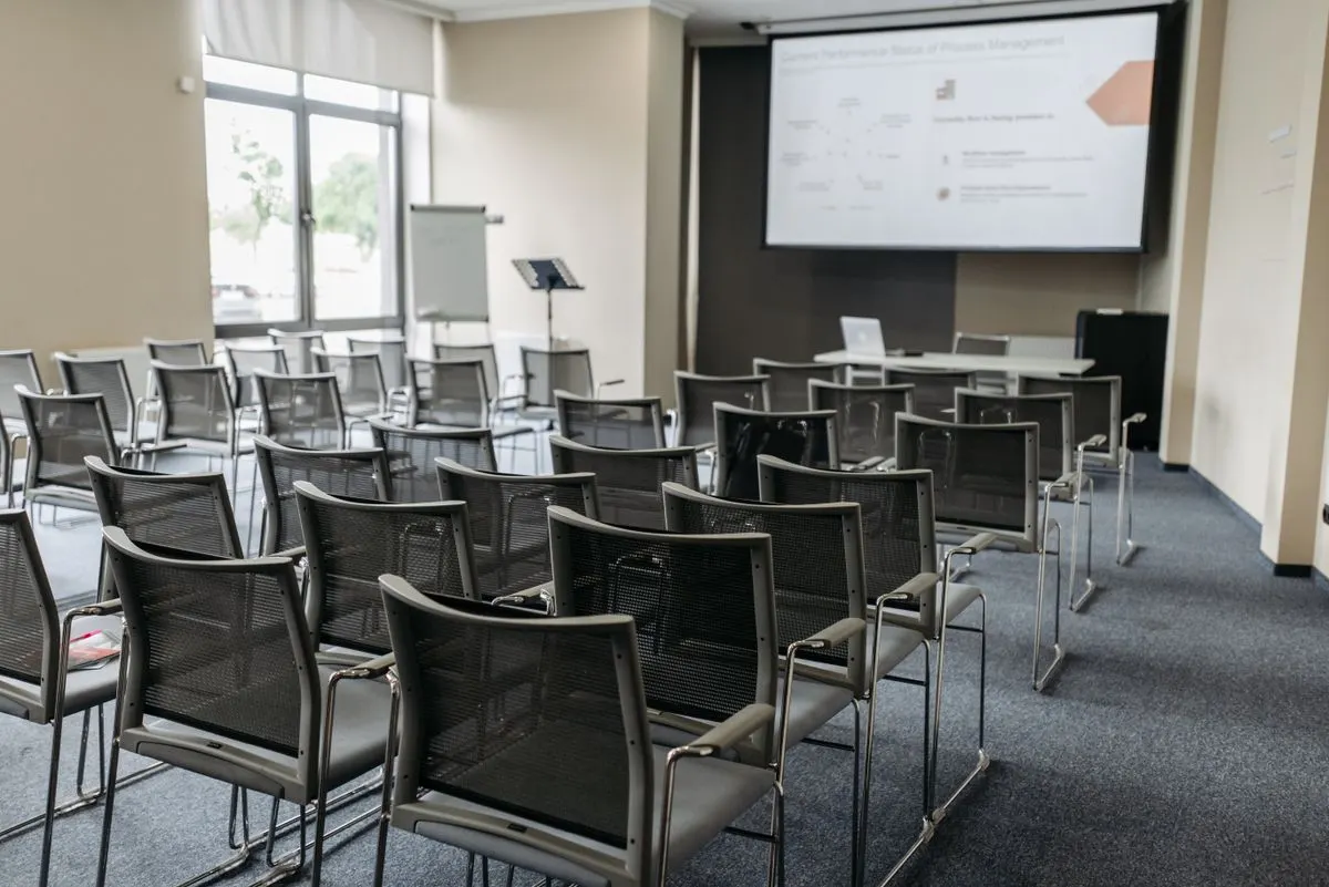 Pusta sala konferencyjna z ekranem projekcyjnym i laptopem na stole prelegenta — Cykliczne szkolenia odświeżające wiedzę o nowych funkcjach AI