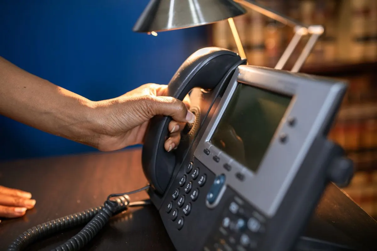 dłoń podnosząca słuchawkę telefonu biurowego, bez twarzy — Kontakt telefoniczny zawsze dostępny w trakcie zlecenia