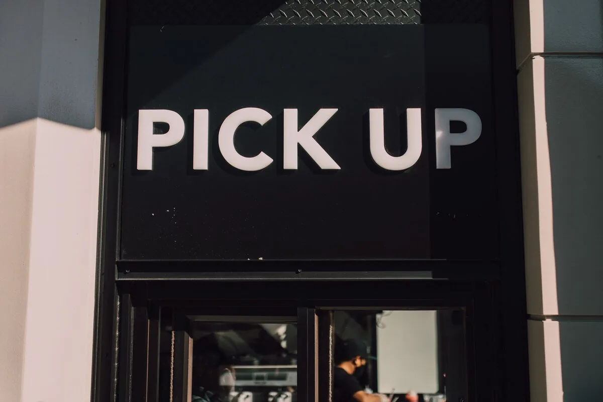 Napis PICK UP nad wejściem do punktu odbioru zamówień — Click &amp; Collect — odbiór zamówień internetowych w sklepie stacjonarnym