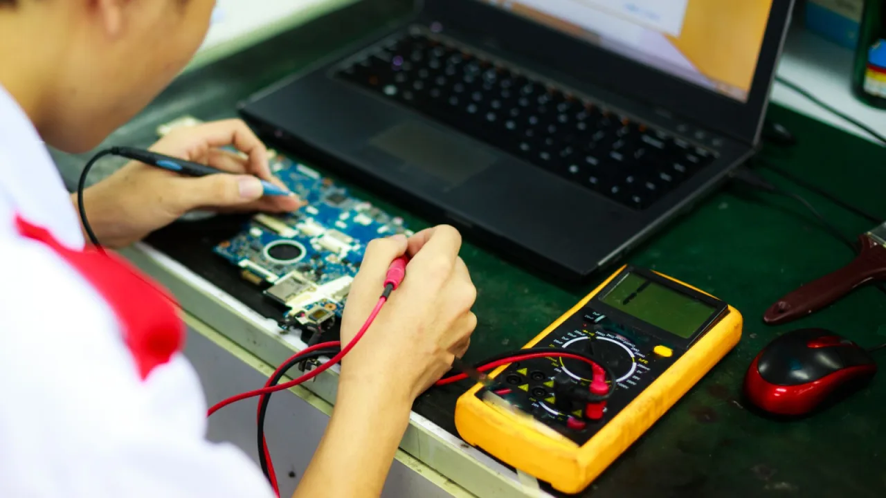 Technik z multimetrem naprawia płytę główną laptopa obok czerwonej myszki — Otwartość na trudne, nietypowe zgłoszenia