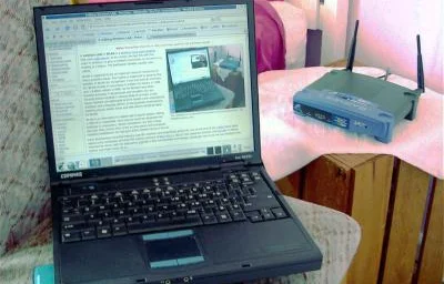 Stary laptop Compaq obok routera bezprzewodowego z dwiema antenami, zdjęcie niskiej rozdzielczości ale czytelne — Konfiguracja sieci pod telefonię satelitarną w lokalizacjach bez naziemnego internetu