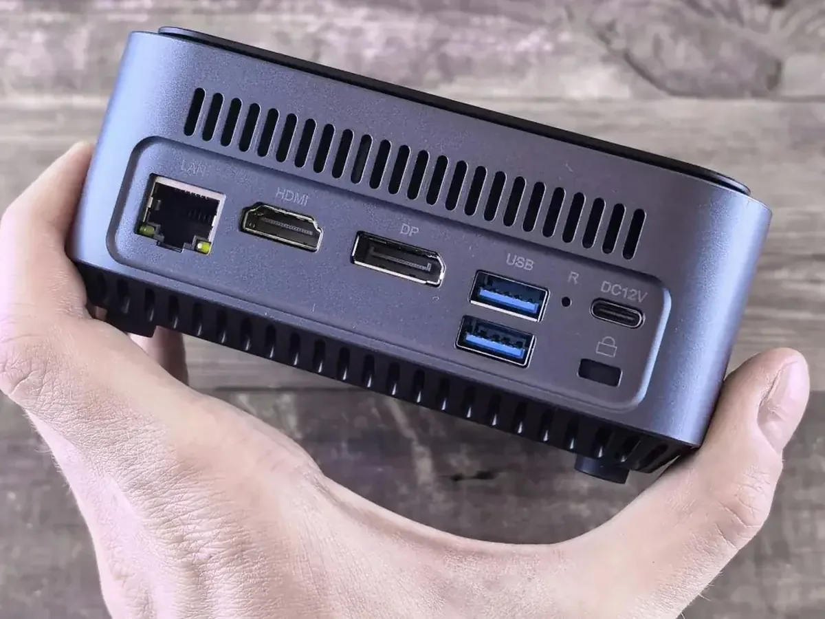 Dłoń trzymająca mini komputer z widocznymi portami LAN, HDMI, DP i USB