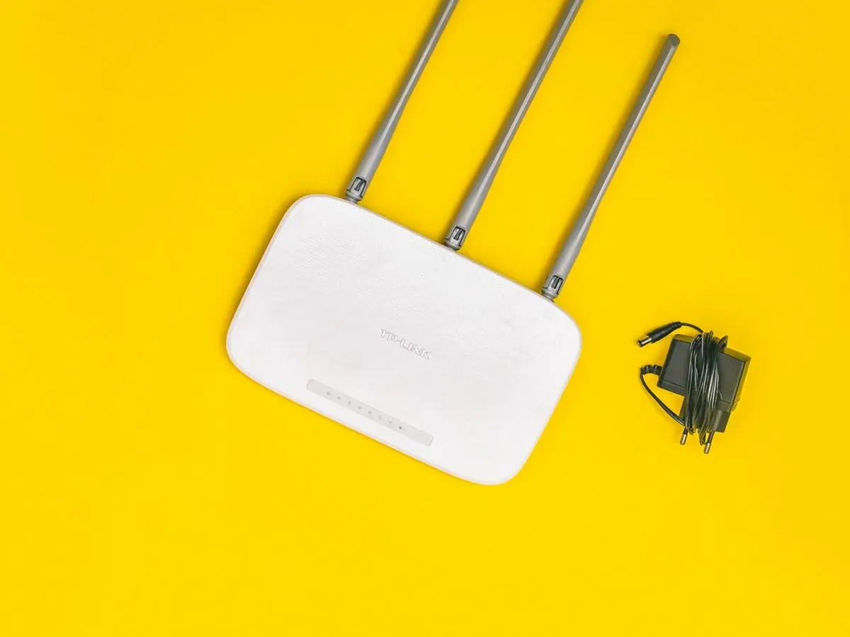 Biały router TP-Link z trzema antenami i zasilaczem na żółtym tle