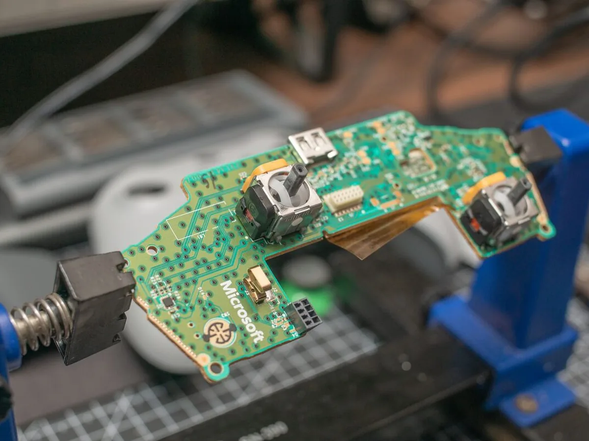 Płytka pada Xbox z logo Microsoft zamocowana w imadle podczas naprawy