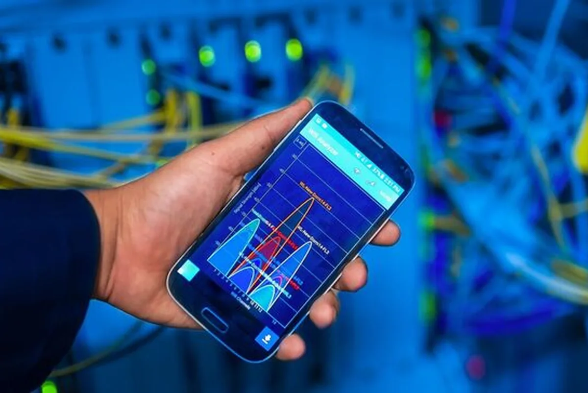Dłoń trzymająca telefon z aplikacją WiFi Analyzer na tle serwerowni