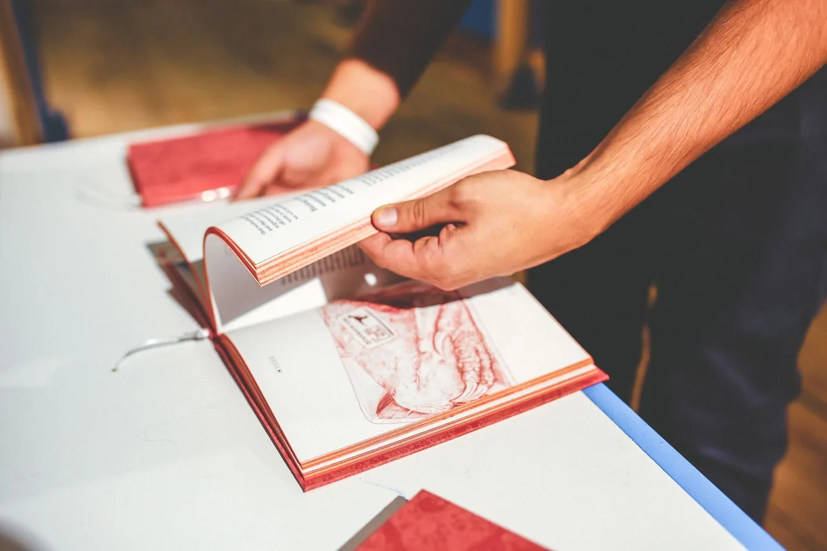 Close-up of a person flipping through a book at a desk indoors.
