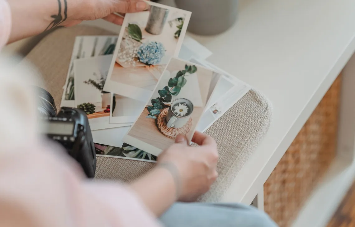From above anonymous photographer looking through printed photos placed on white table in living room