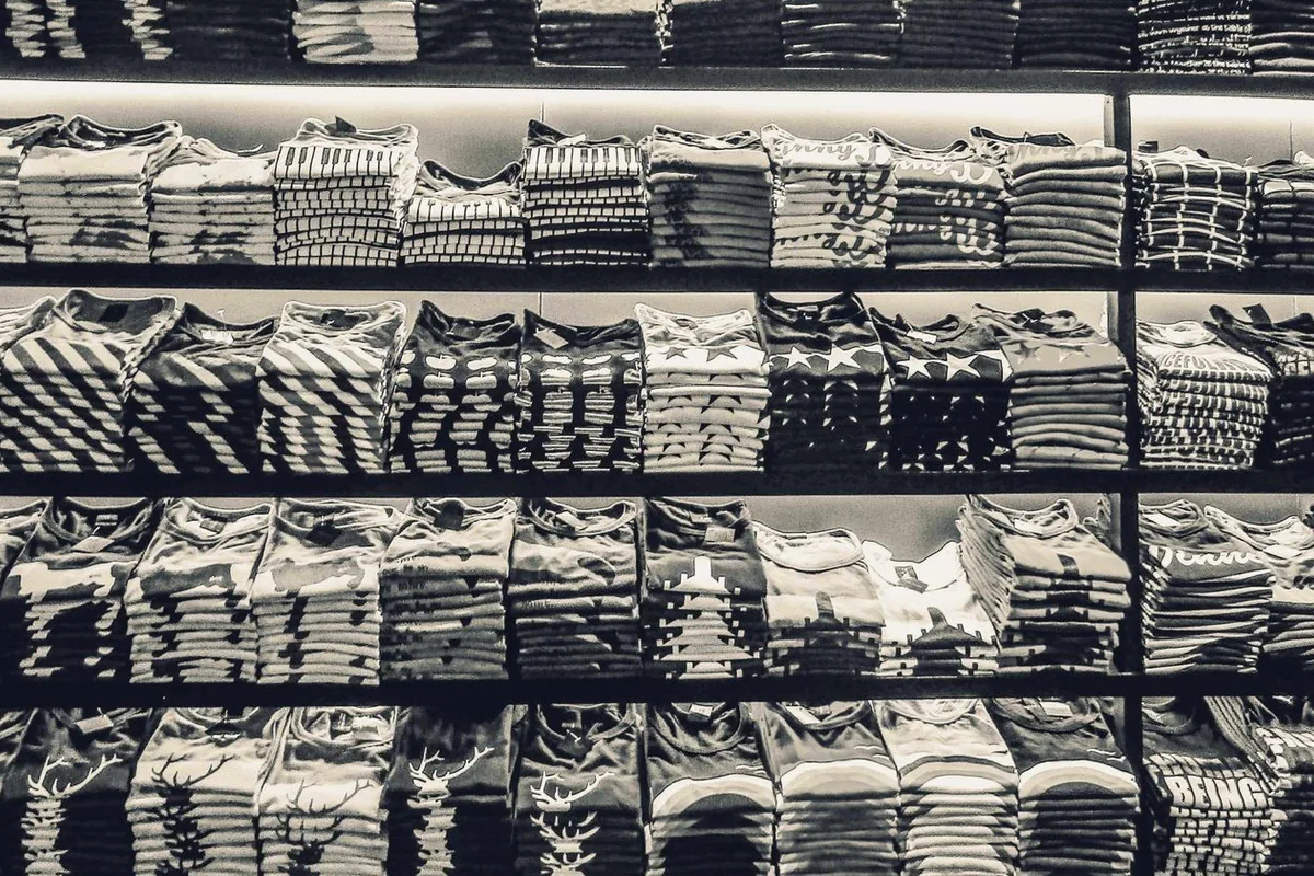 Black and white image showcasing neatly folded t-shirts stacked on store shelves.