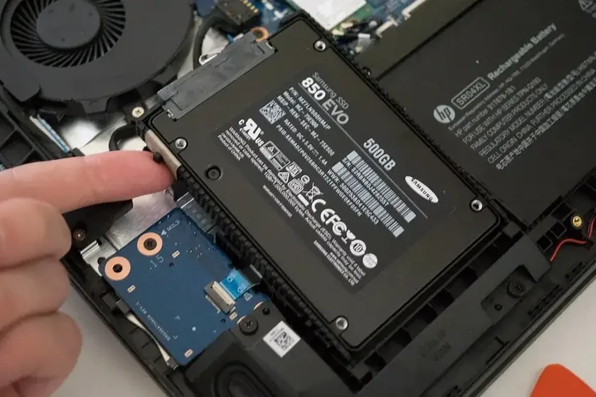 Palec przy dysku SSD Samsung 850 EVO montowanym obok oryginalnej baterii HP