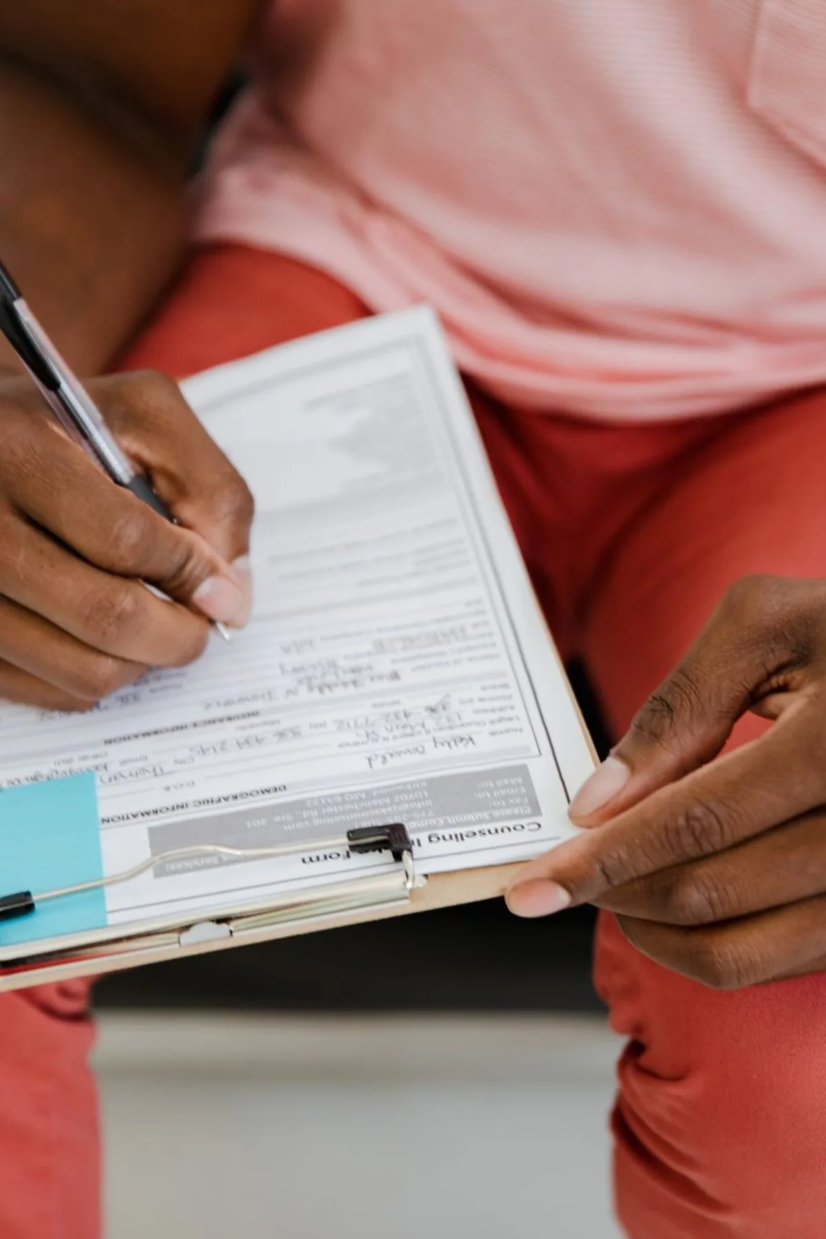 Close-up of a hand writing on a form with a pen attached to a clipboard.