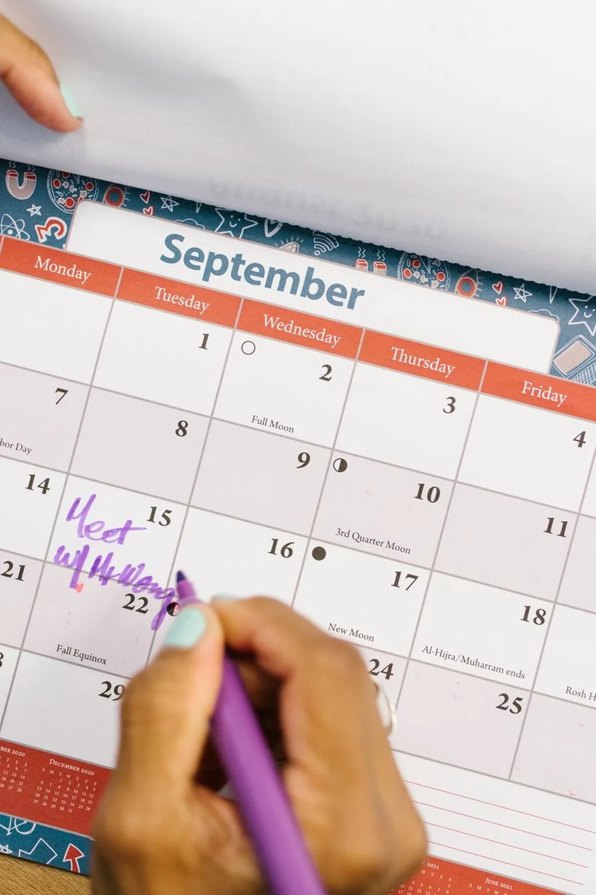 A person marking a calendar in September with a purple pen on a wooden desk.