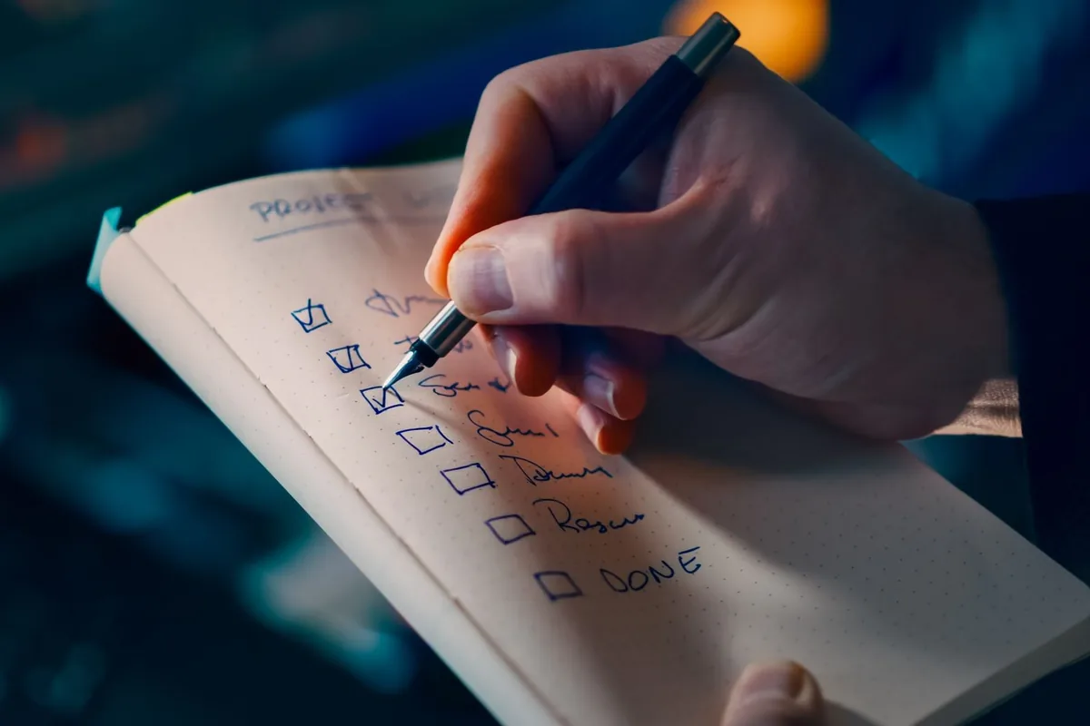 Close-up of a hand writing a checklist in a notebook, symbolizing productivity and organization.