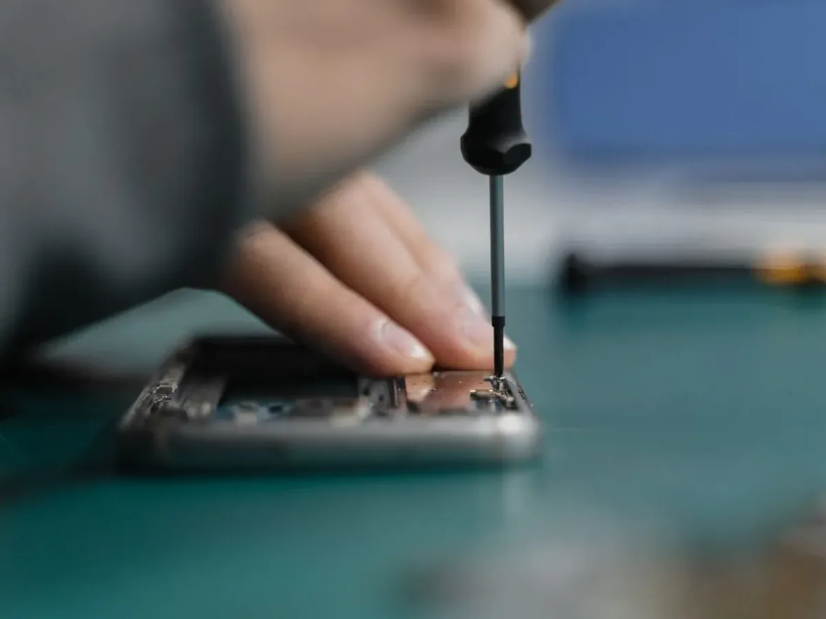 Dłonie naprawiające rozebrany telefon śrubokrętem precyzyjnym