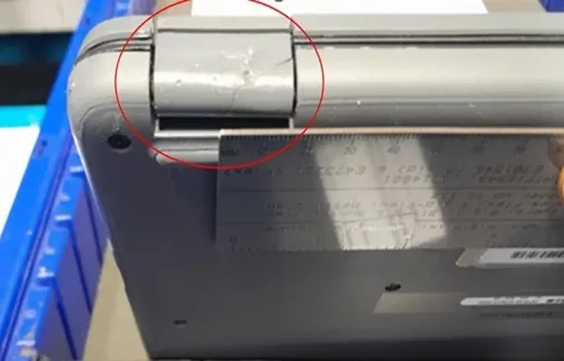Zarysowany i pogięty zawias laptopa zaznaczony czerwonym kółkiem, laptop w magazynie