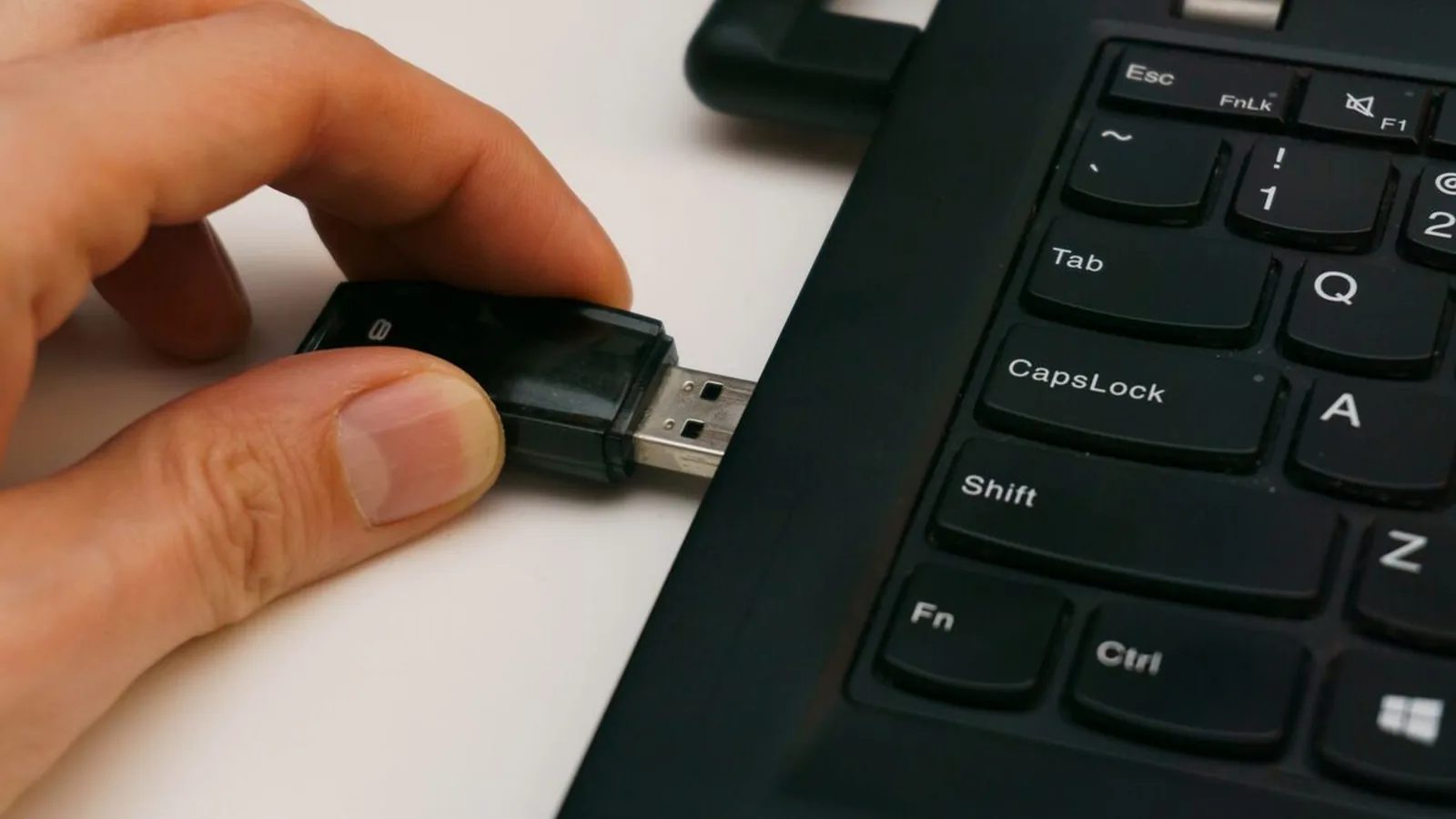 Dłoń wkładająca pendrive do portu USB laptopa typu ThinkPad