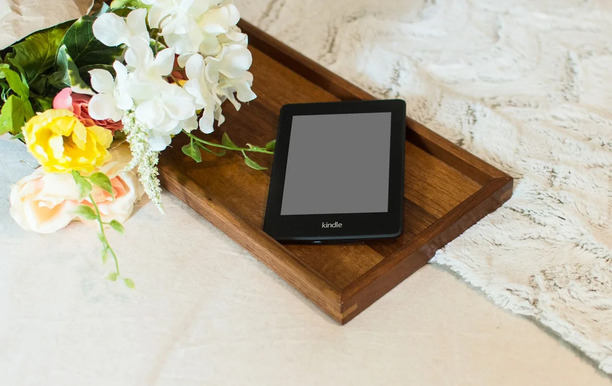 czytnik Kindle na drewnianej tacy obok kwiatów — Amazon Kindle Paperwhite 3 w zgłoszeniu — jak odpowiadamy i co radzimy