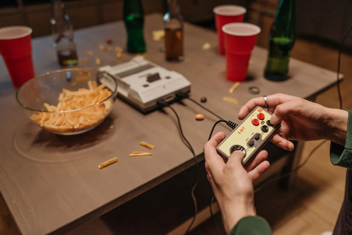dłonie trzymające kontroler retro obok przekąsek i napojów — Atari 2600 a zakres naszego serwisu — czym zajmujemy się zamiast