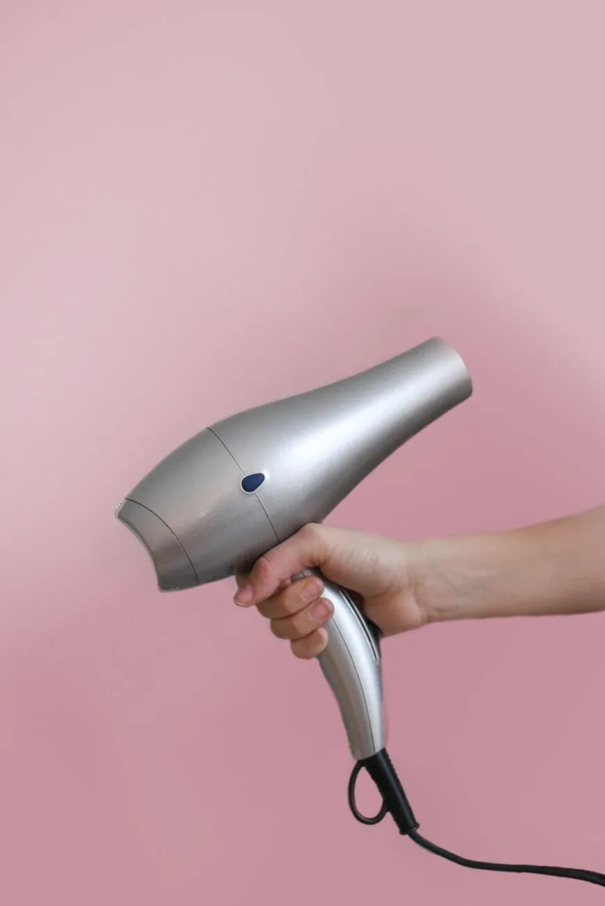 dłoń trzymająca srebrną suszarkę na różowym tle — Babyliss Steam Pure — czego przy tym sprzęcie nie zrobimy