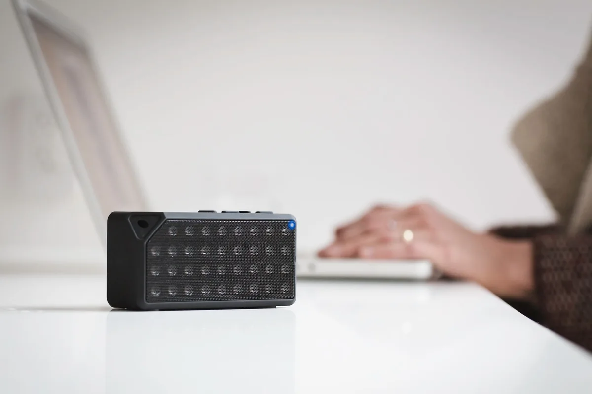 głośnik bezprzewodowy obok laptopa na białym biurku — Dlaczego nie bierzemy Audio Pro C10 do naprawy