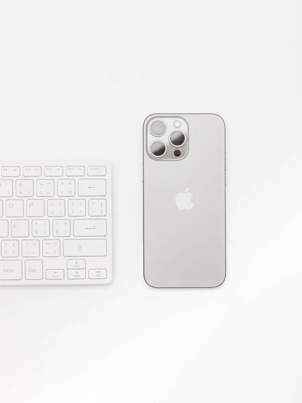 srebrny iPhone obok białej klawiatury na białym tle — Dlaczego nie bierzemy iPhone 16 Plus do naprawy