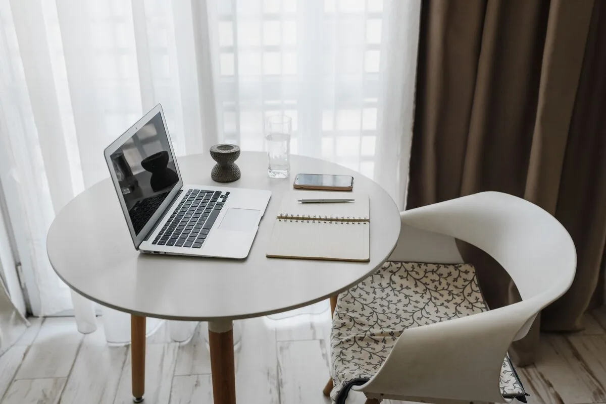 MacBook Air na okrągłym stoliku przy oknie z notatnikiem i telefonem — Dlaczego nie bierzemy MacBook Air M2 15 cali (2023) do naprawy