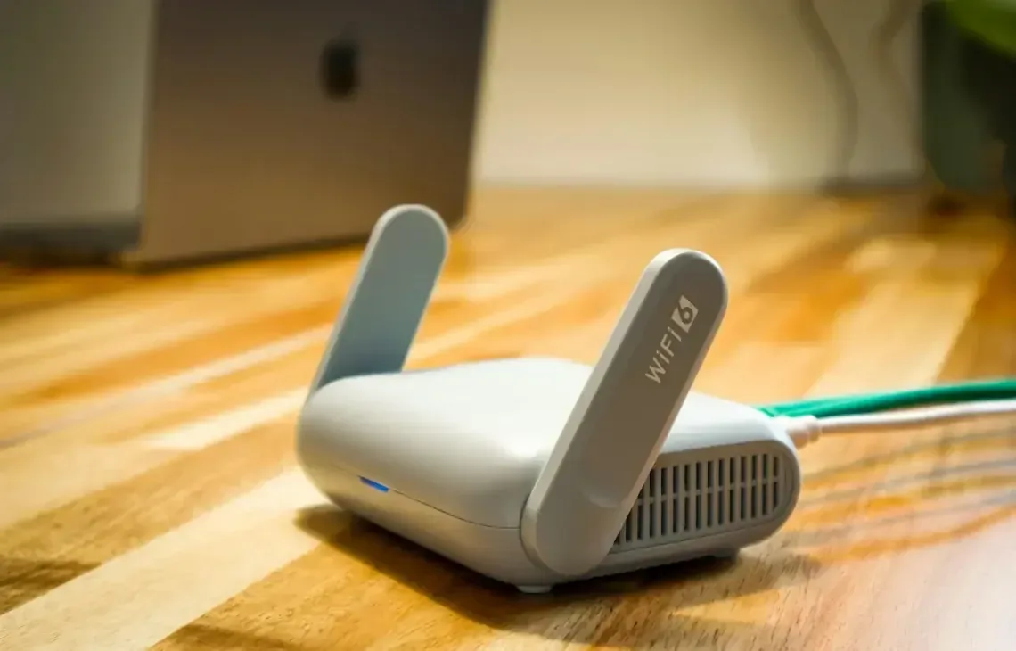 router WiFi na podłodze przy rozmytym laptopie Apple w tle — Dlaczego nie bierzemy MacBook Pro 16 cali (2019) do naprawy