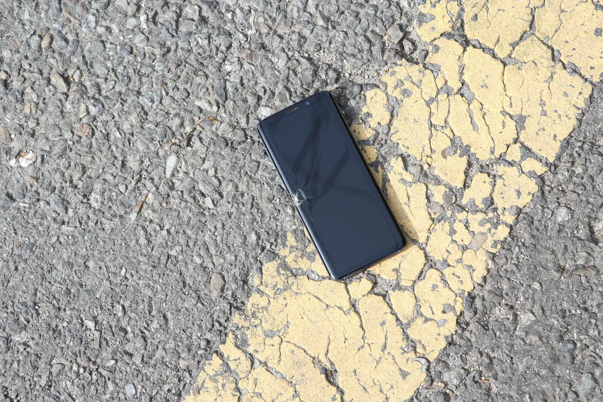pęknięty smartfon leżący na nasłonecznionej asfaltowej drodze — Dlaczego nie bierzemy Nokia 3210 do naprawy