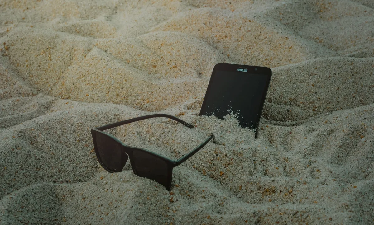smartfon i okulary przeciwsłoneczne w piasku — Dlaczego nie bierzemy POCO X7 Pro do naprawy