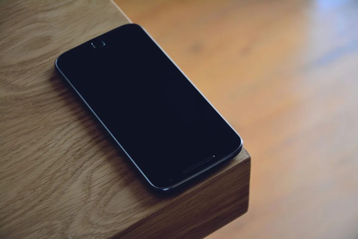 smartfon leżący na krawędzi drewnianego stołu — Dlaczego nie bierzemy Samsung Galaxy A03 Core do naprawy