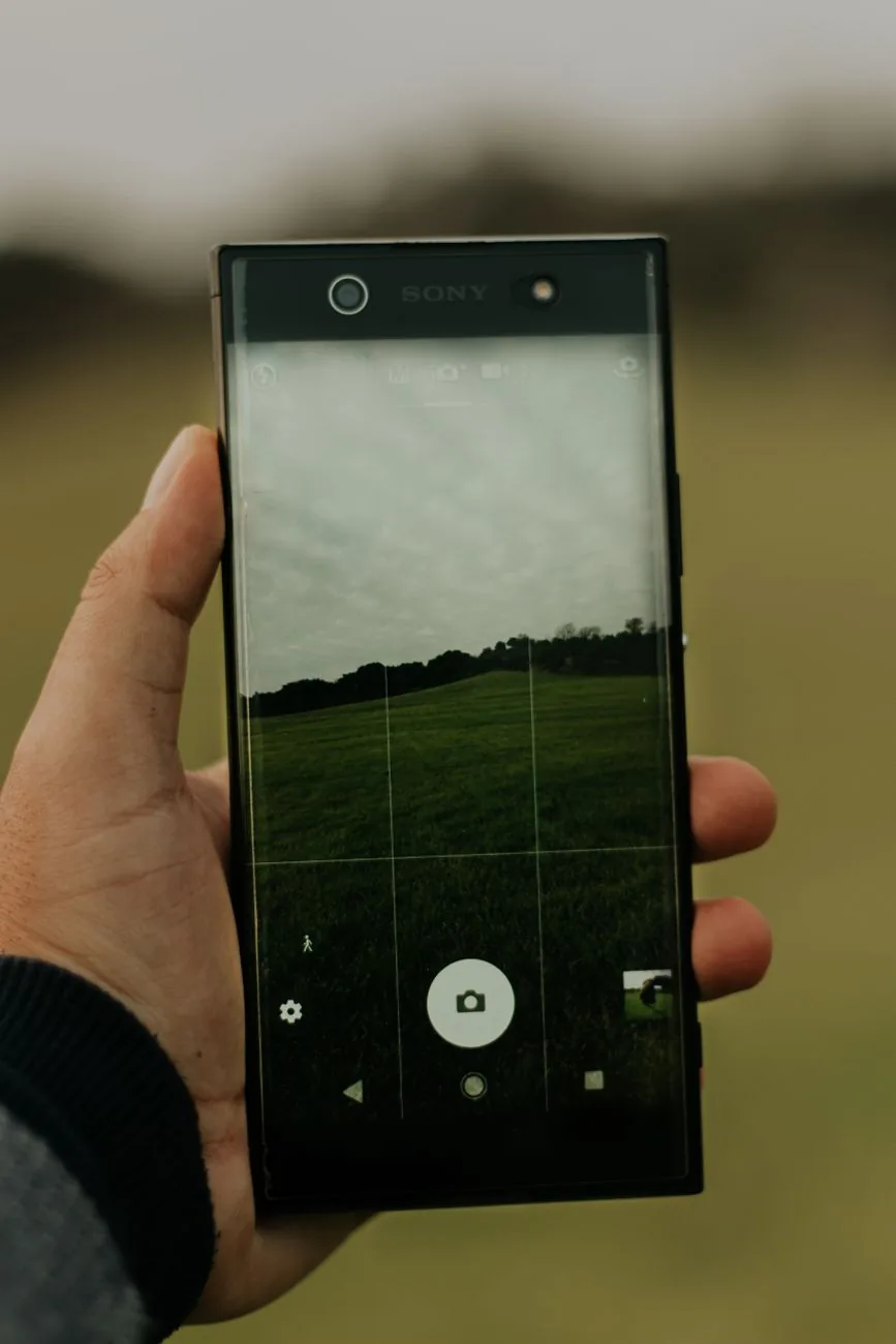dłoń trzymająca smartfon z podglądem aparatu na trawiaste pole — Dlaczego nie bierzemy Samsung Galaxy S6 do naprawy