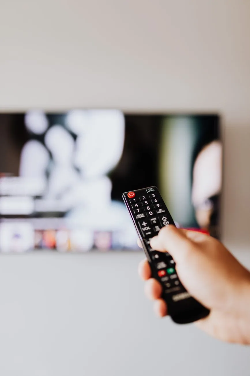 dłoń z pilotem skierowanym w stronę telewizora — Hisense U8NQ poza naszym warsztatem — gdzie szukać pomocy