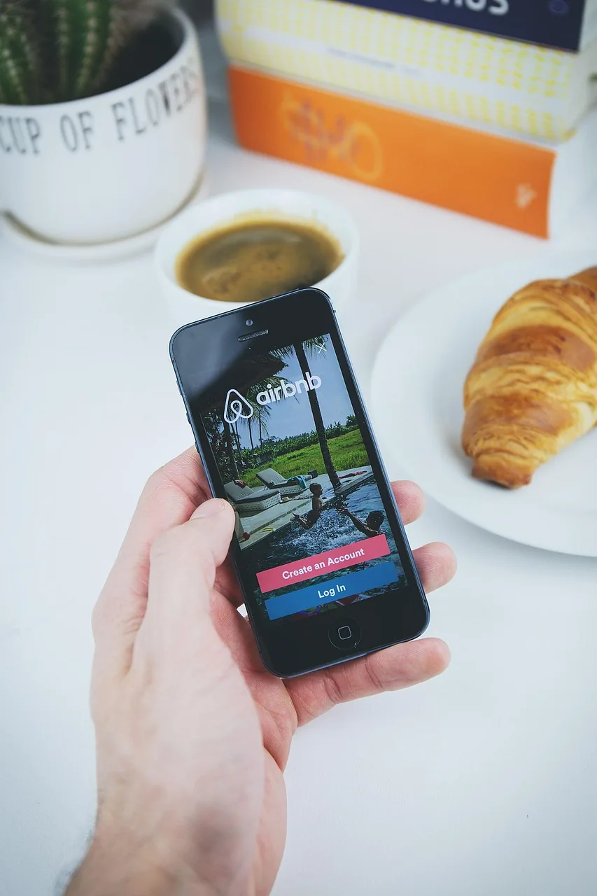 dłoń trzymająca iPhone nad stołem z kawą i croissantem — iPhone 17 poza naszym warsztatem — gdzie szukać pomocy