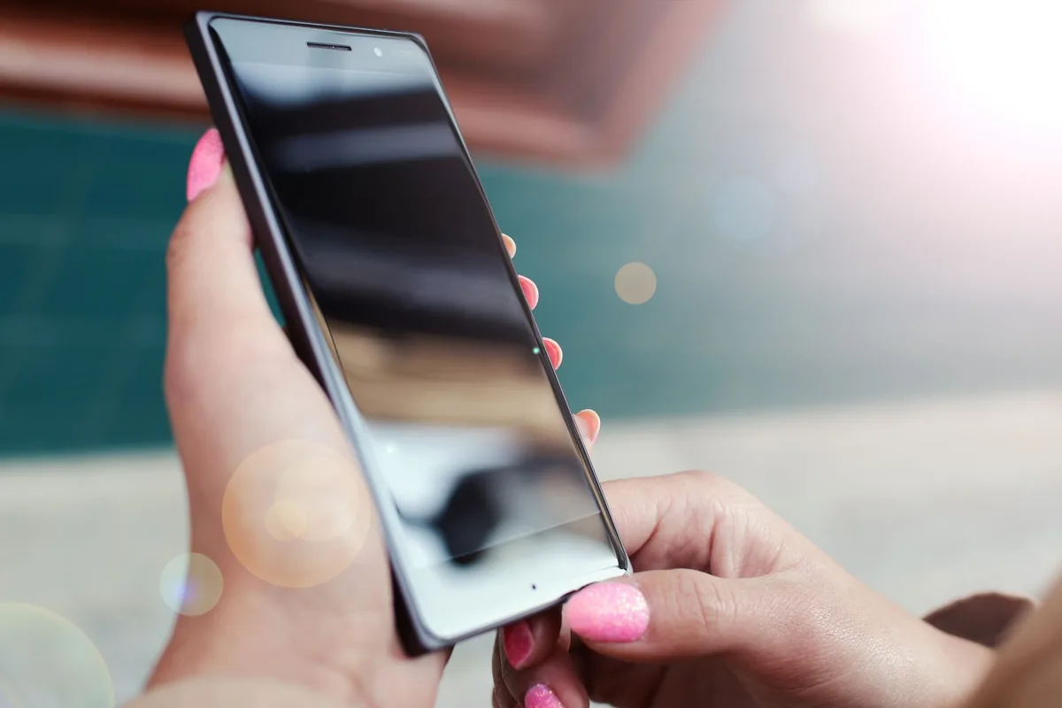 dłonie trzymające telefon komórkowy w pełnym słońcu — LG K42 a zakres naszego serwisu — czym zajmujemy się zamiast