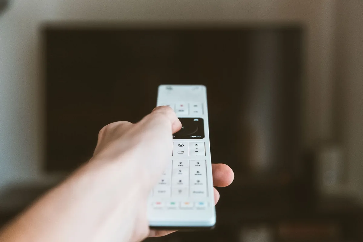 dłoń trzymająca pilot skierowany w stronę telewizora — LG OLED G4 poza naszym warsztatem — gdzie szukać pomocy
