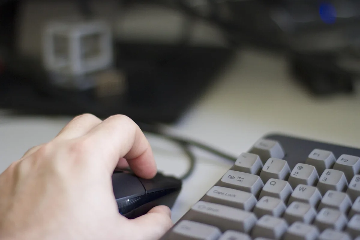 dłoń na myszy komputerowej obok szarej klawiatury — Logitech G402 a zakres naszego serwisu — czym zajmujemy się zamiast
