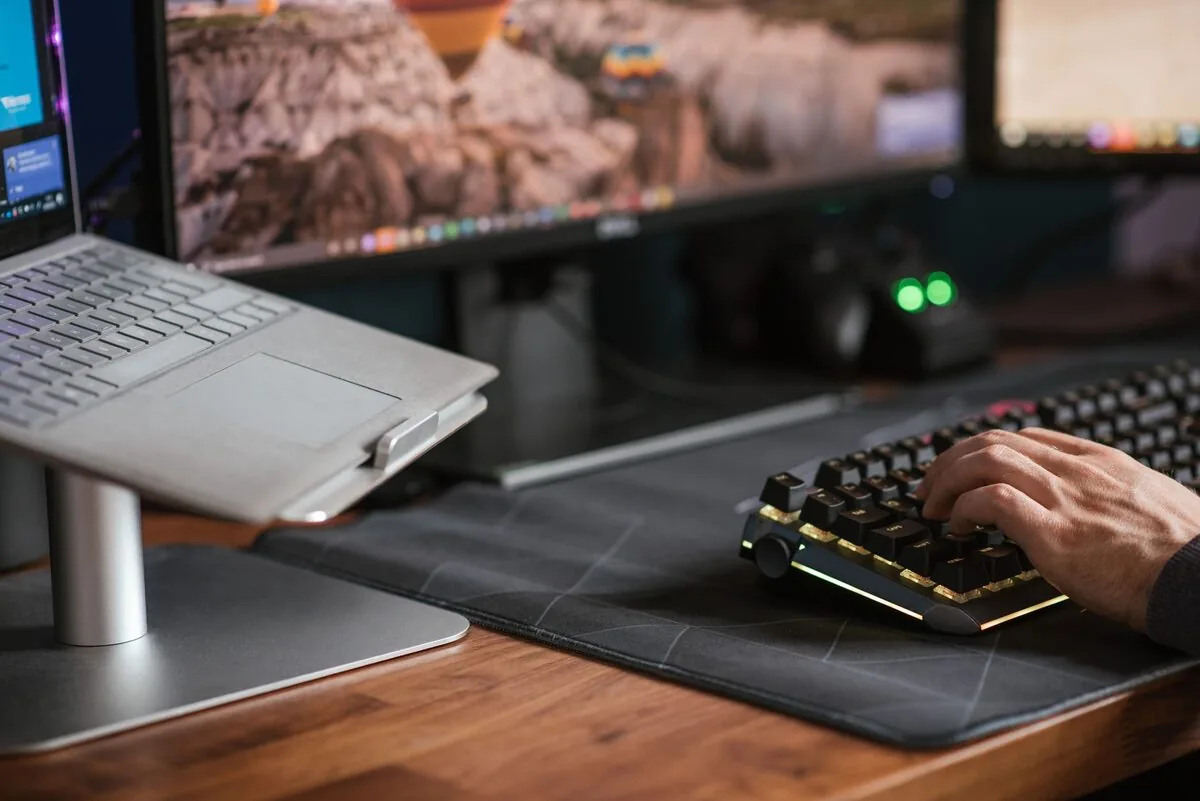 Srebrne urządzenie typu Microsoft Surface z klawiaturą na biurku obok drugiego monitora — Mac mini M2 (2023) w zgłoszeniu — jak odpowiadamy i co radzimy