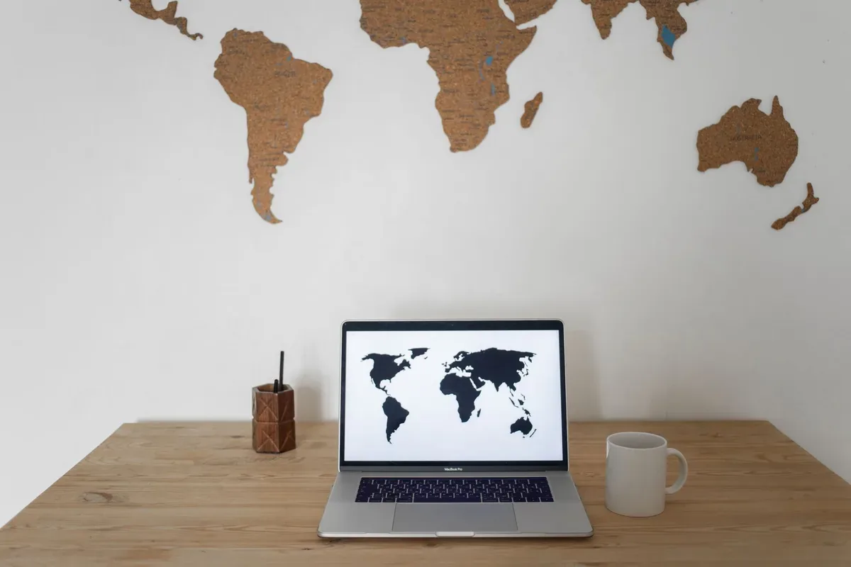 MacBook na drewnianym biurku z mapą świata na ścianie — MacBook Air 11 cali (2013) a zakres naszego serwisu — czym zajmujemy się zamiast