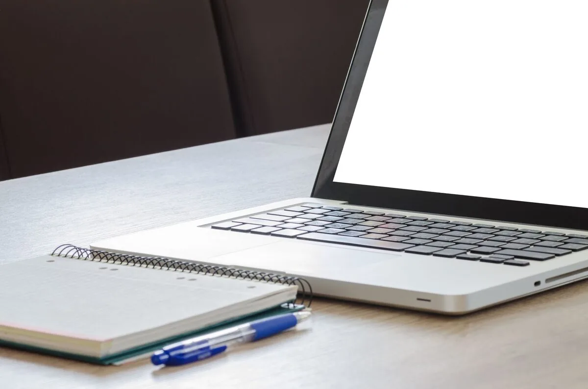 Otwarty MacBook z pustym białym ekranem obok notatnika i długopisów — MacBook Air M2 13 cali (2022) a zakres naszego serwisu — czym zajmujemy się zamiast