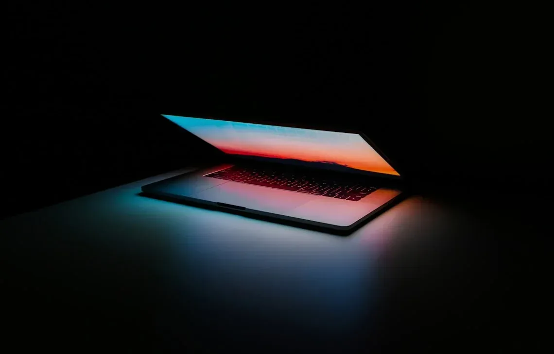 Otwarty laptop MacBook z kolorową tapetą na ekranie w ciemnym pomieszczeniu — MacBook Pro 15 cali (2019) a zakres naszego serwisu — czym zajmujemy się zamiast