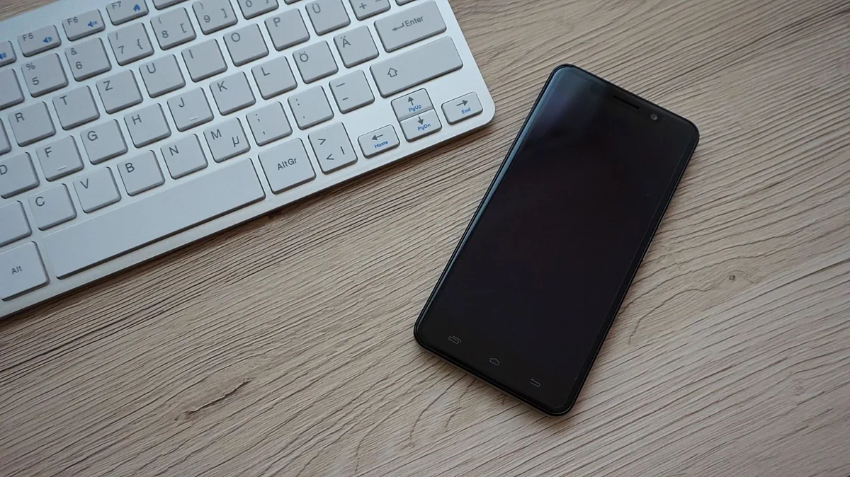 telefon komórkowy obok klawiatury na drewnianym biurku — Nothing Phone 1 a zakres naszego serwisu — czym zajmujemy się zamiast