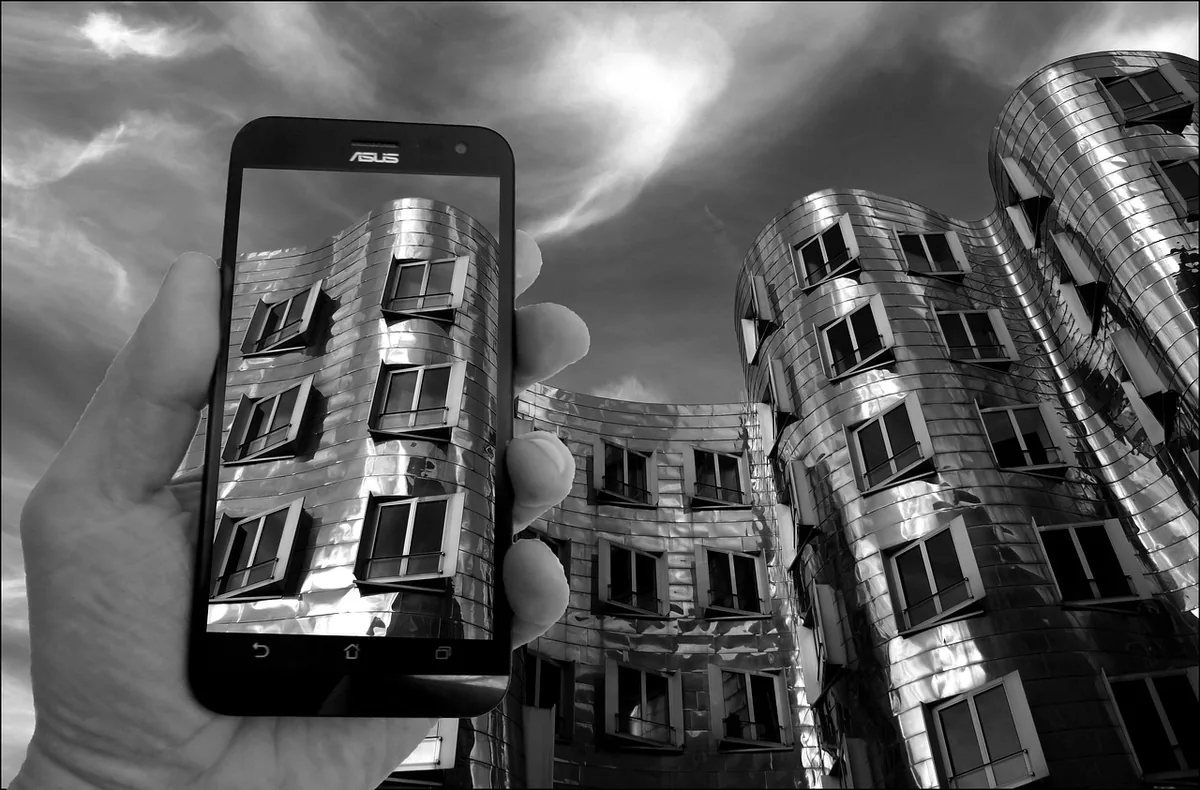 dłoń trzymająca smartfon na tle nowoczesnego wieżowca — OnePlus 9 Pro poza naszym warsztatem — gdzie szukać pomocy