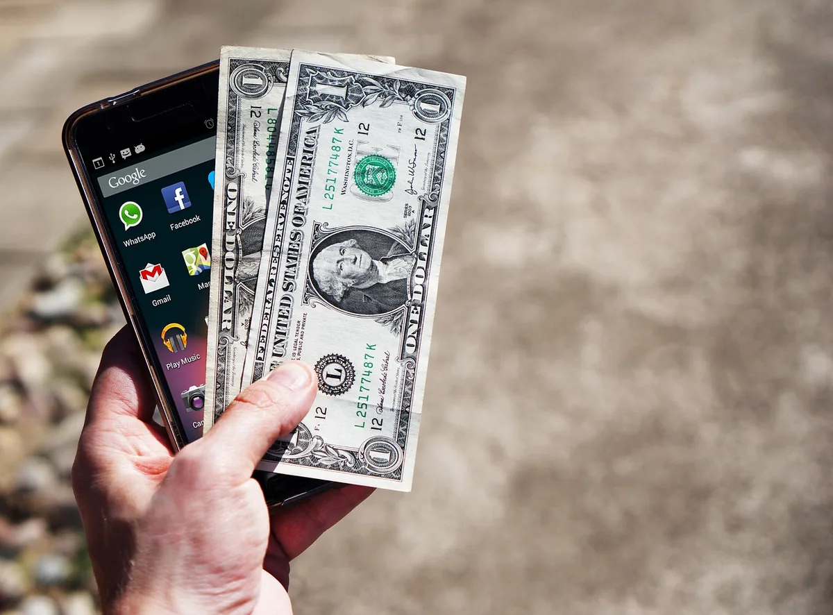 smartfon leżący obok amerykańskich banknotów dolarowych — OPPO Reno 4 a zakres naszego serwisu — czym zajmujemy się zamiast