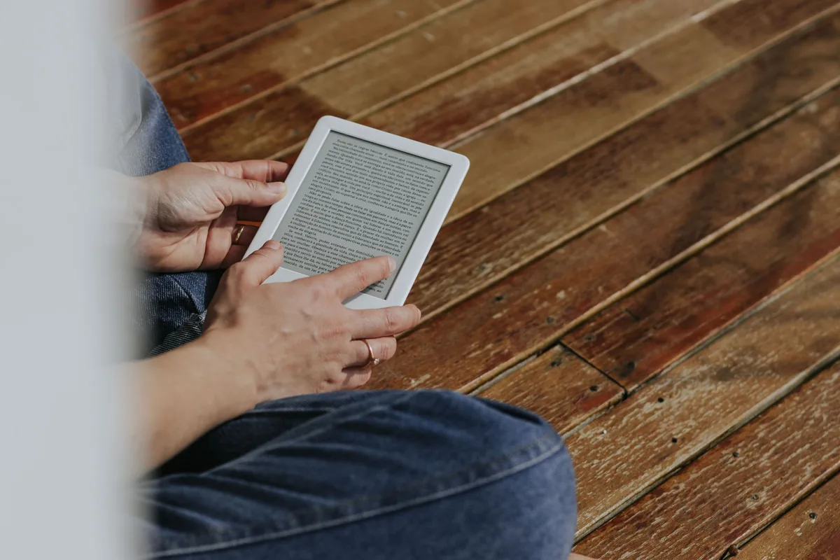 dłonie trzymające czytnik e-booków nad drewnianą podłogą — PocketBook Touch Lux 5 w zgłoszeniu — jak odpowiadamy i co radzimy