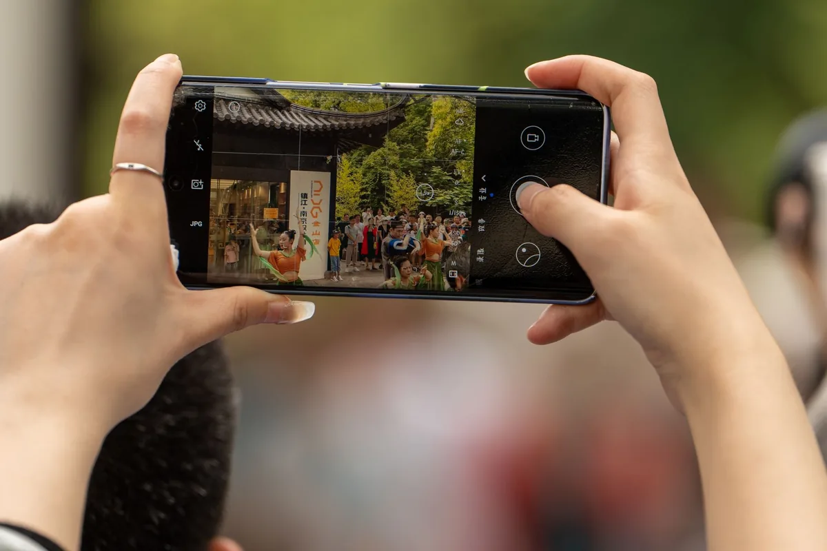 dłonie trzymające smartfon podczas plenerowego wydarzenia kulturalnego — realme 5i a zakres naszego serwisu — czym zajmujemy się zamiast