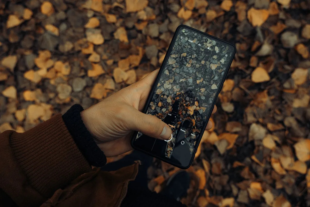 dłoń trzymająca smartfon nad jesiennymi liśćmi — Samsung Galaxy A10 a zakres naszego serwisu — czym zajmujemy się zamiast