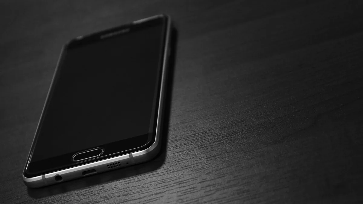 czarny smartfon leżący na ciemnym drewnianym stole — Samsung Galaxy Z Flip a zakres naszego serwisu — czym zajmujemy się zamiast
