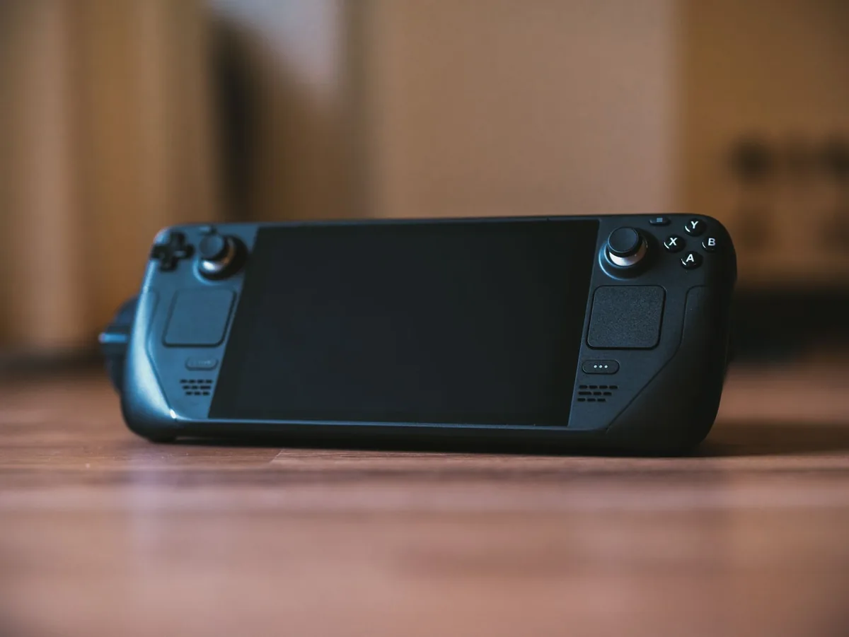 przenośna konsola z joystickiem na drewnianym stole — Steam Deck OLED poza naszym warsztatem — gdzie szukać pomocy